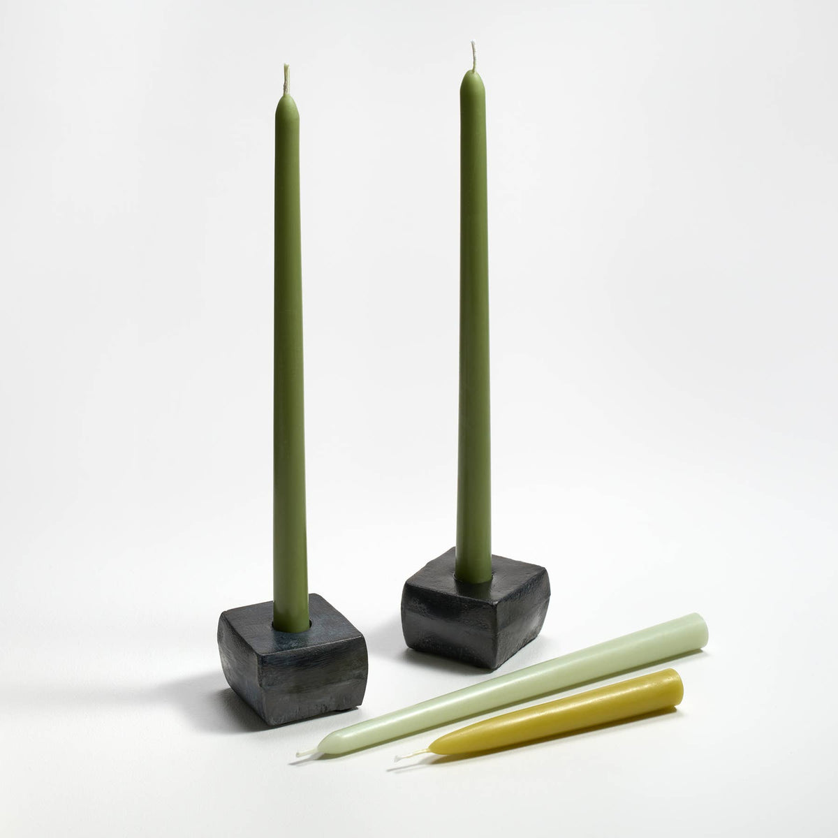 Two black square candle holders with green candles on a white background