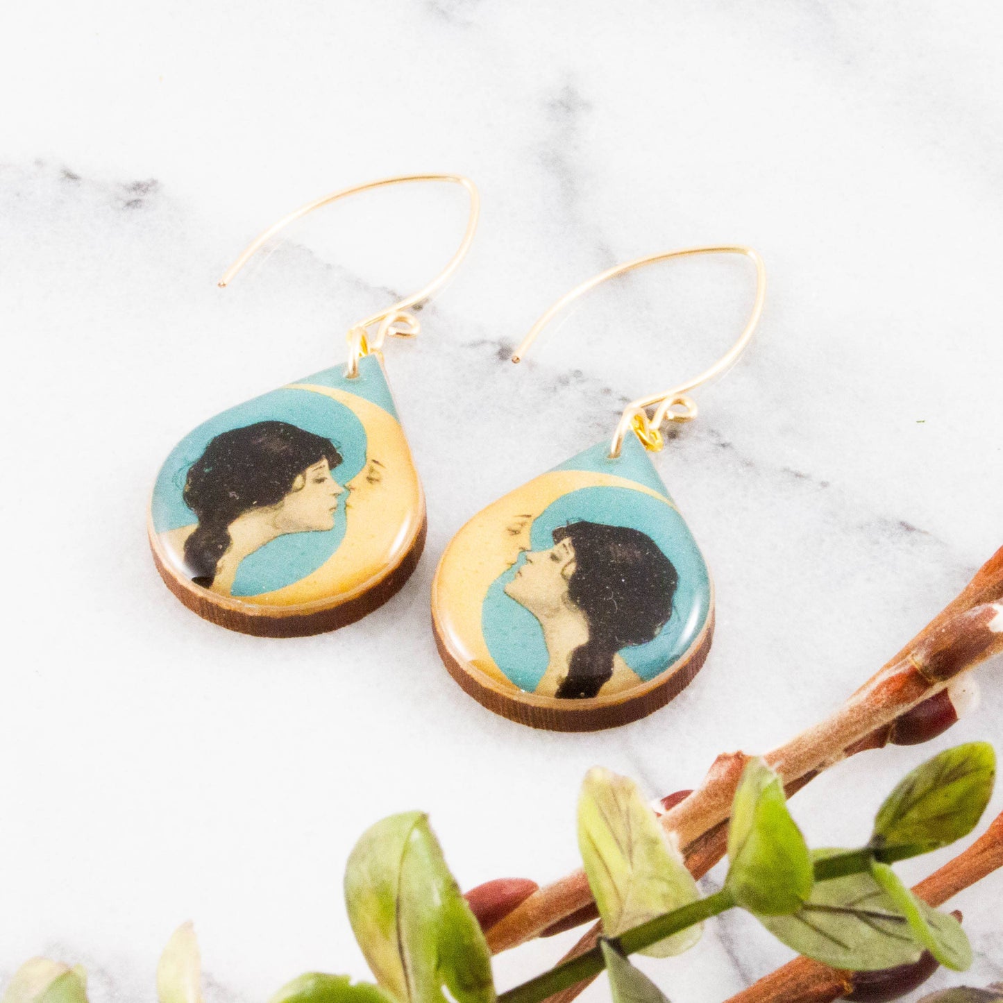 Pair of earrings with artistic design on a marble surface with leaves.