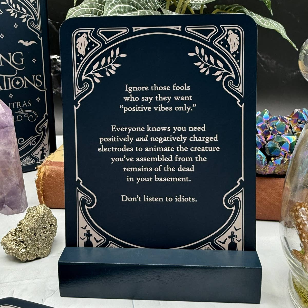 Decorative card with a humorous quote on a stand, surrounded by mystical items.