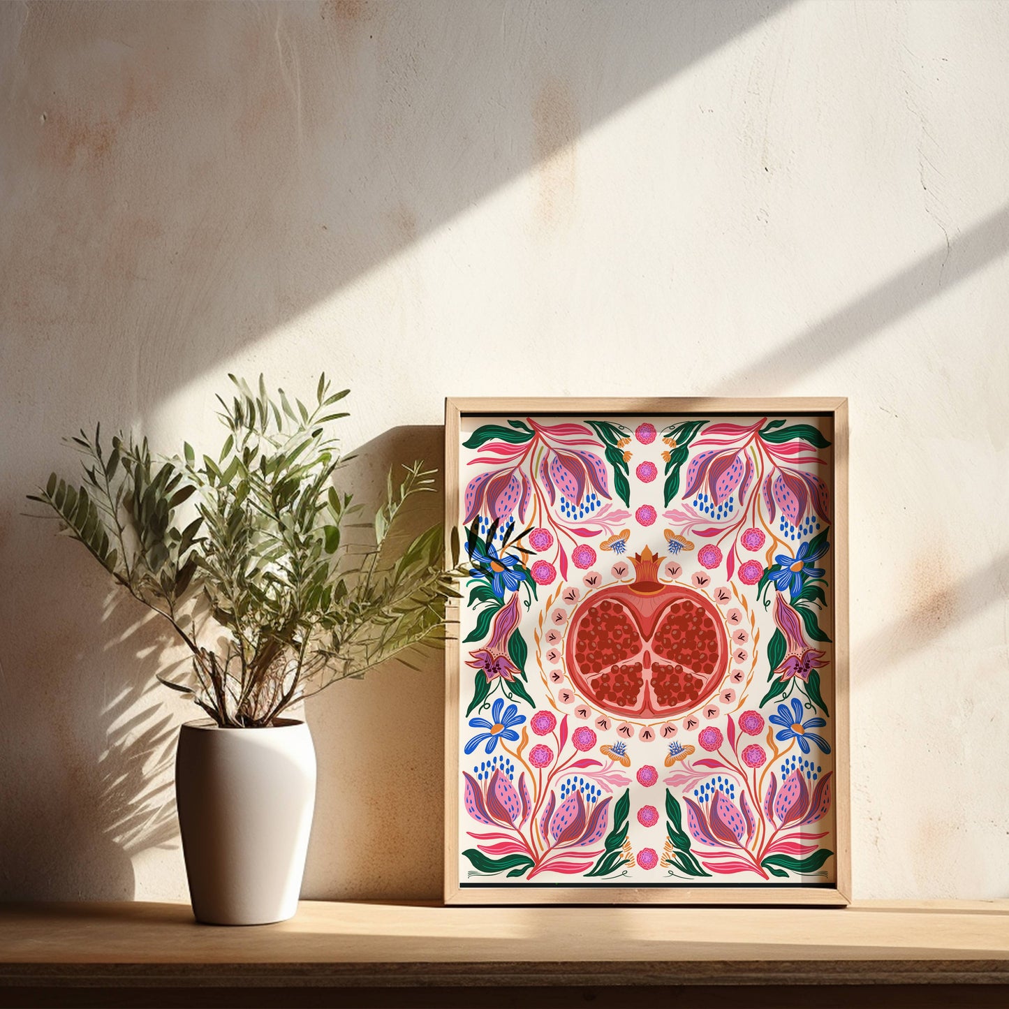Colorful pomegranate art print in wood frame leaning against wall.