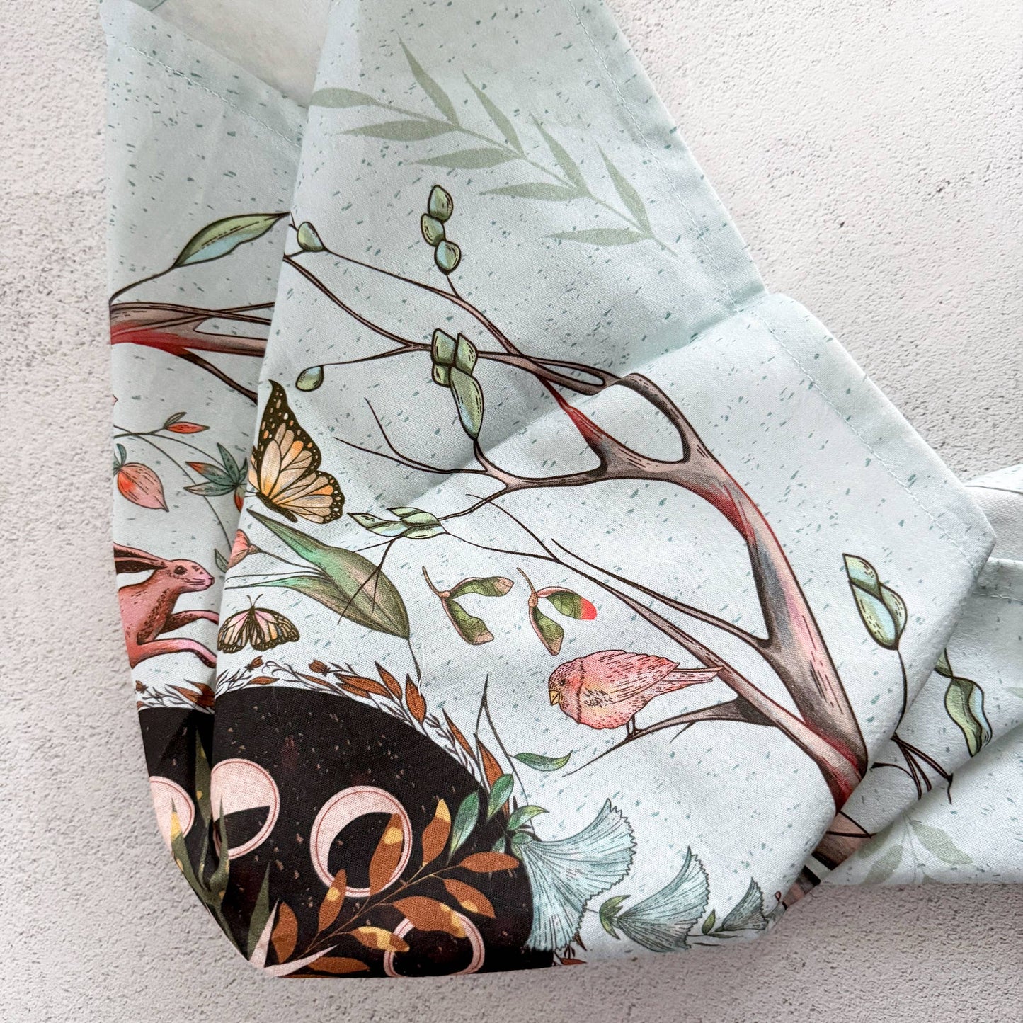 Folded fabric with nature-themed design featuring trees, birds, and butterflies on a light background.