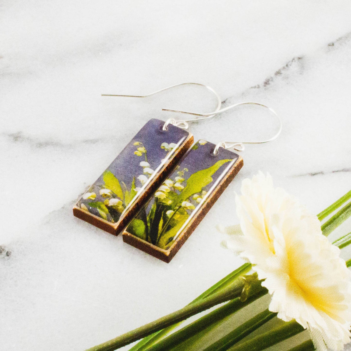 Floral earrings on a marble surface with a white flower.