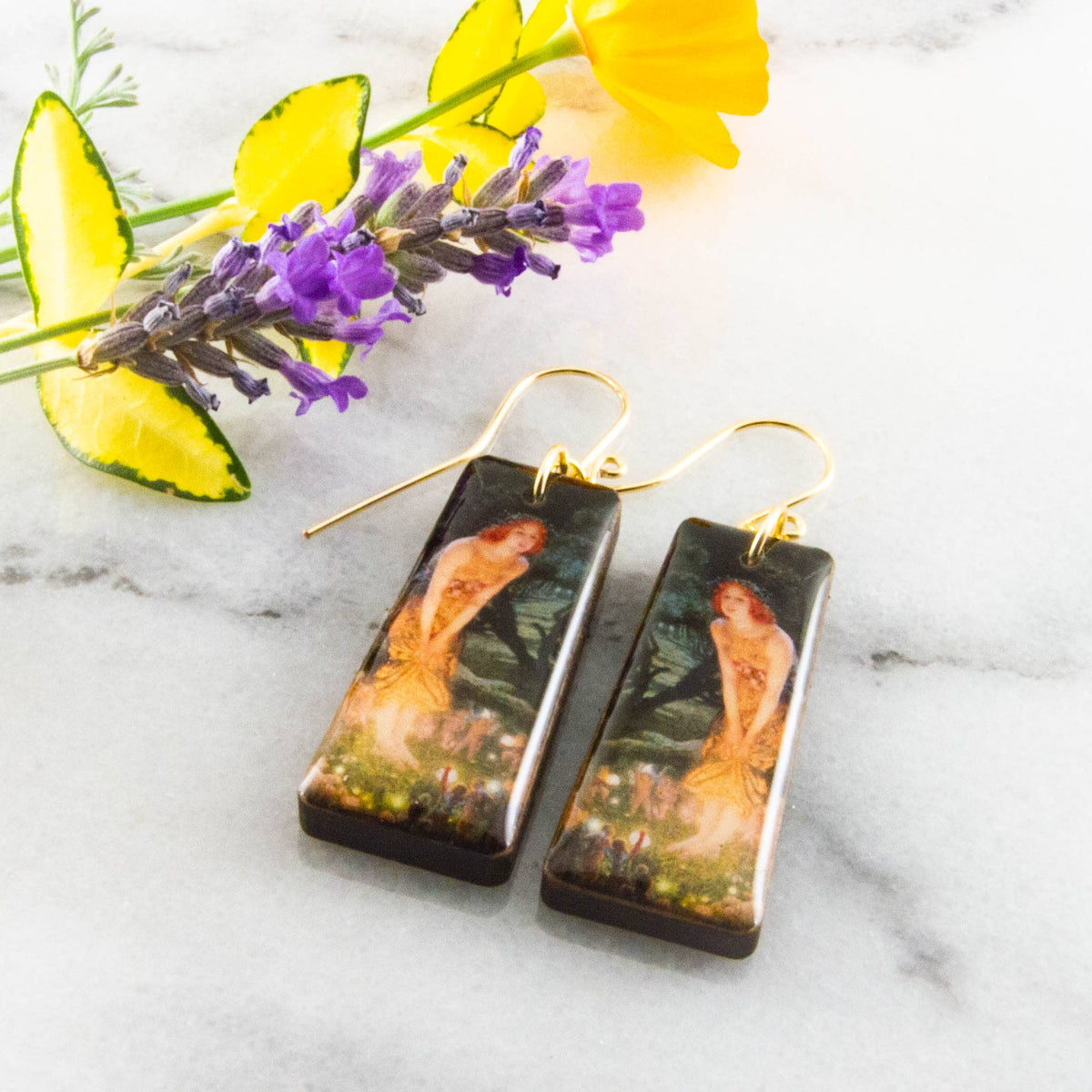 Pair of earrings with artistic design on a marble surface with flowers.