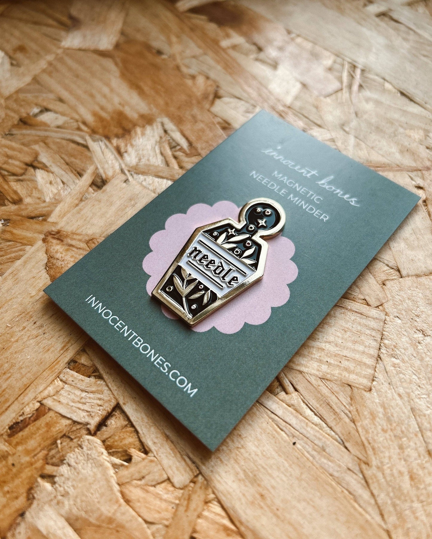 Pin on a card with 'Innocent Bones' branding on a wooden surface