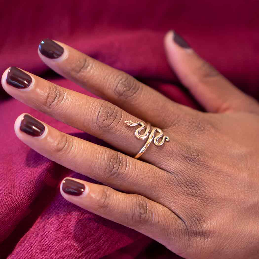 Hand wearing a gold ring with a leaf design against a red fabric background