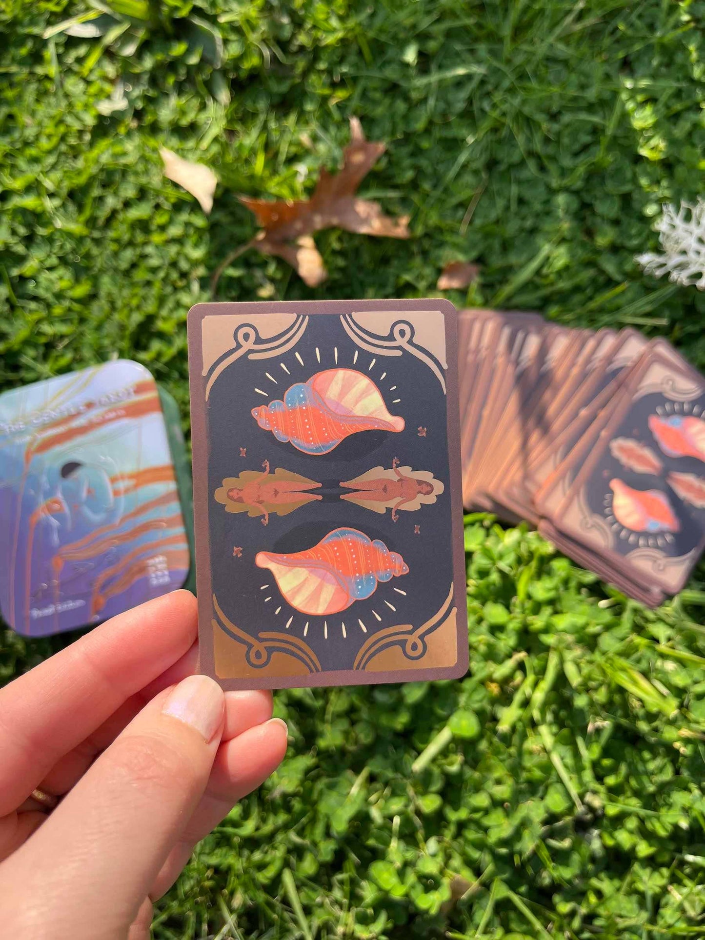 Hand holding a playing card with shell design on grass