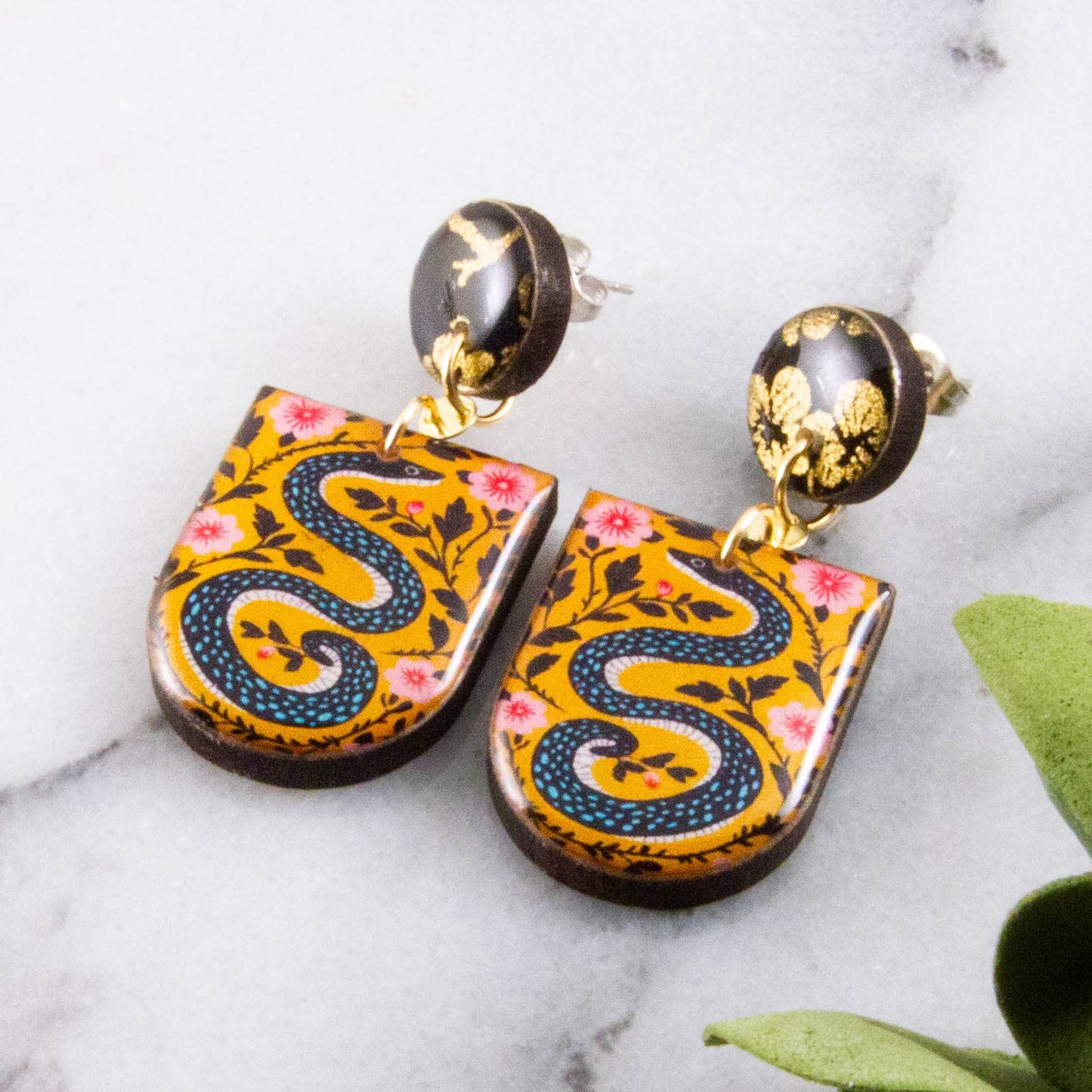 Pair of decorative earrings with snake design on a marble surface