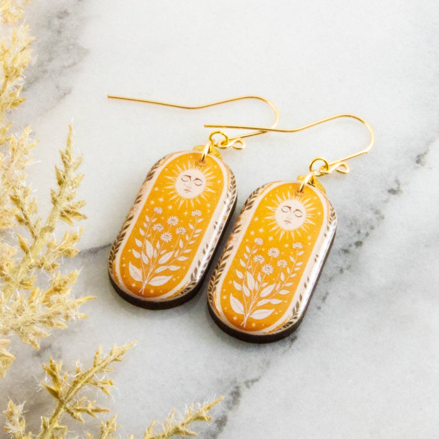 Yellow floral earrings on a marble surface with decorative plants.