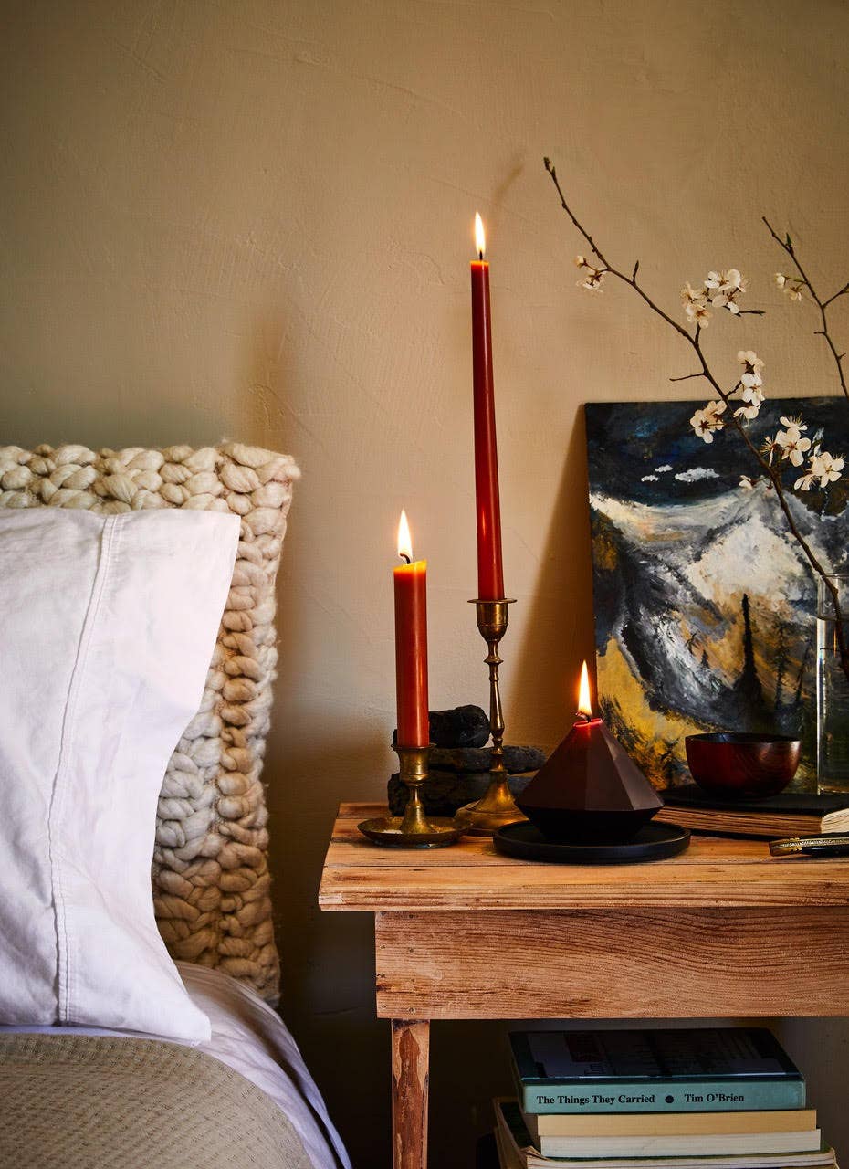 Candlelit scene with candles on a wooden table next to a bed