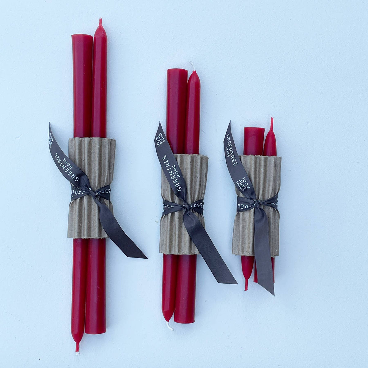 Three bundles of red taper candles wrapped in brown kraft paper bands with black ribbons, arranged on a light blue background.