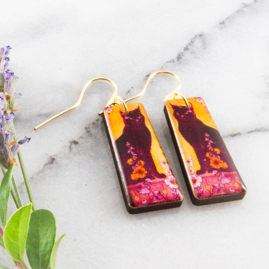 Rectangular earrings with cat design on a marble surface with lavender.