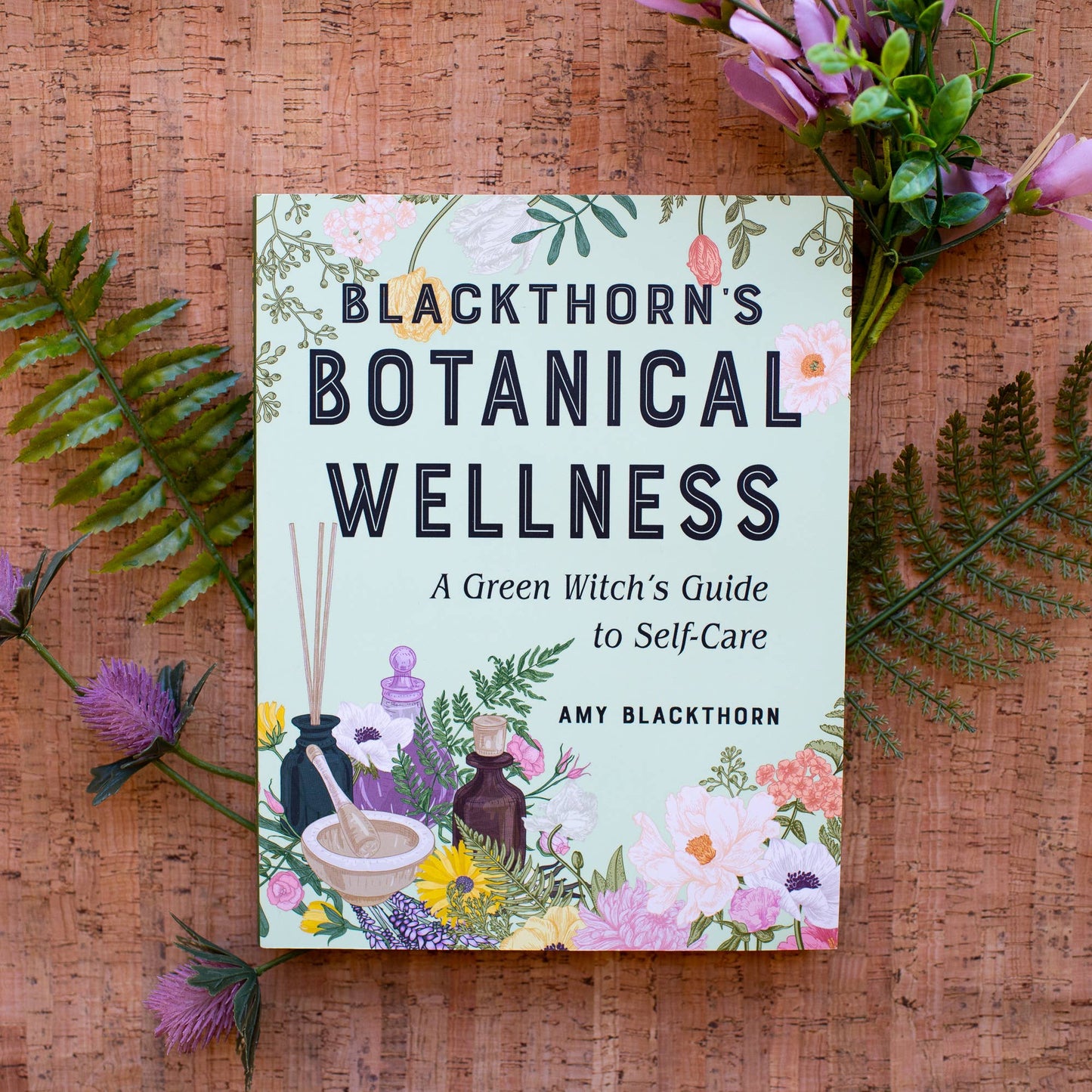 Book titled 'Blackthorn's Botanical Wellness' on a wooden surface with floral decorations.