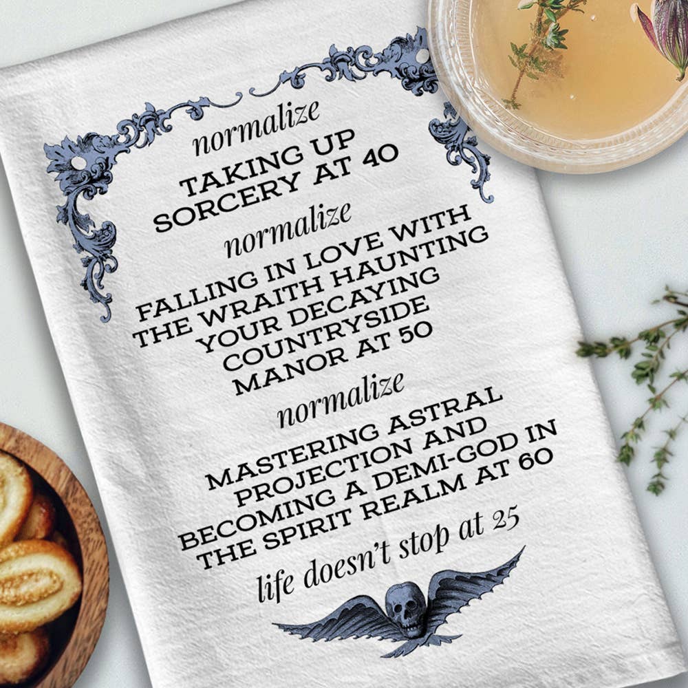 Text on a white towel with decorative elements, placed on a surface with a bowl of cookies and a plant.