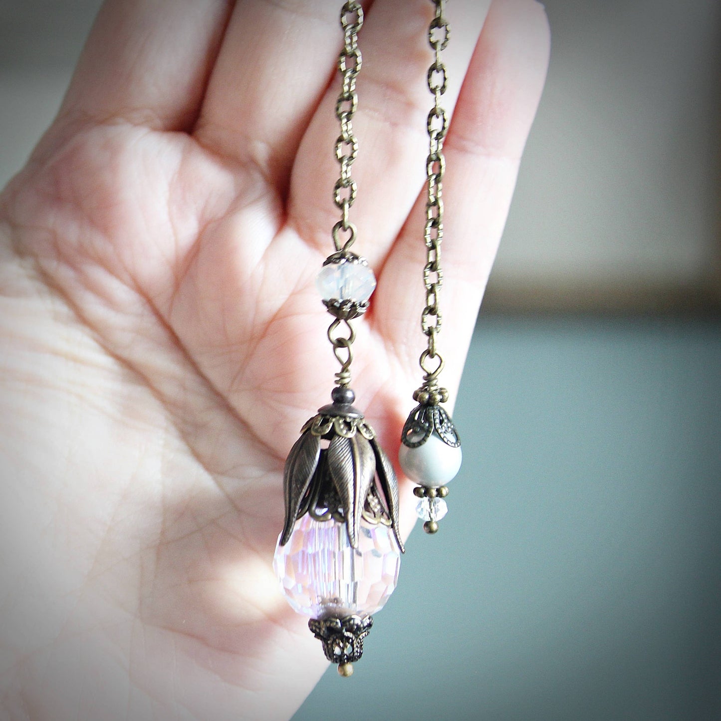 Pendulum with decorative pendants held in a hand against a neutral background