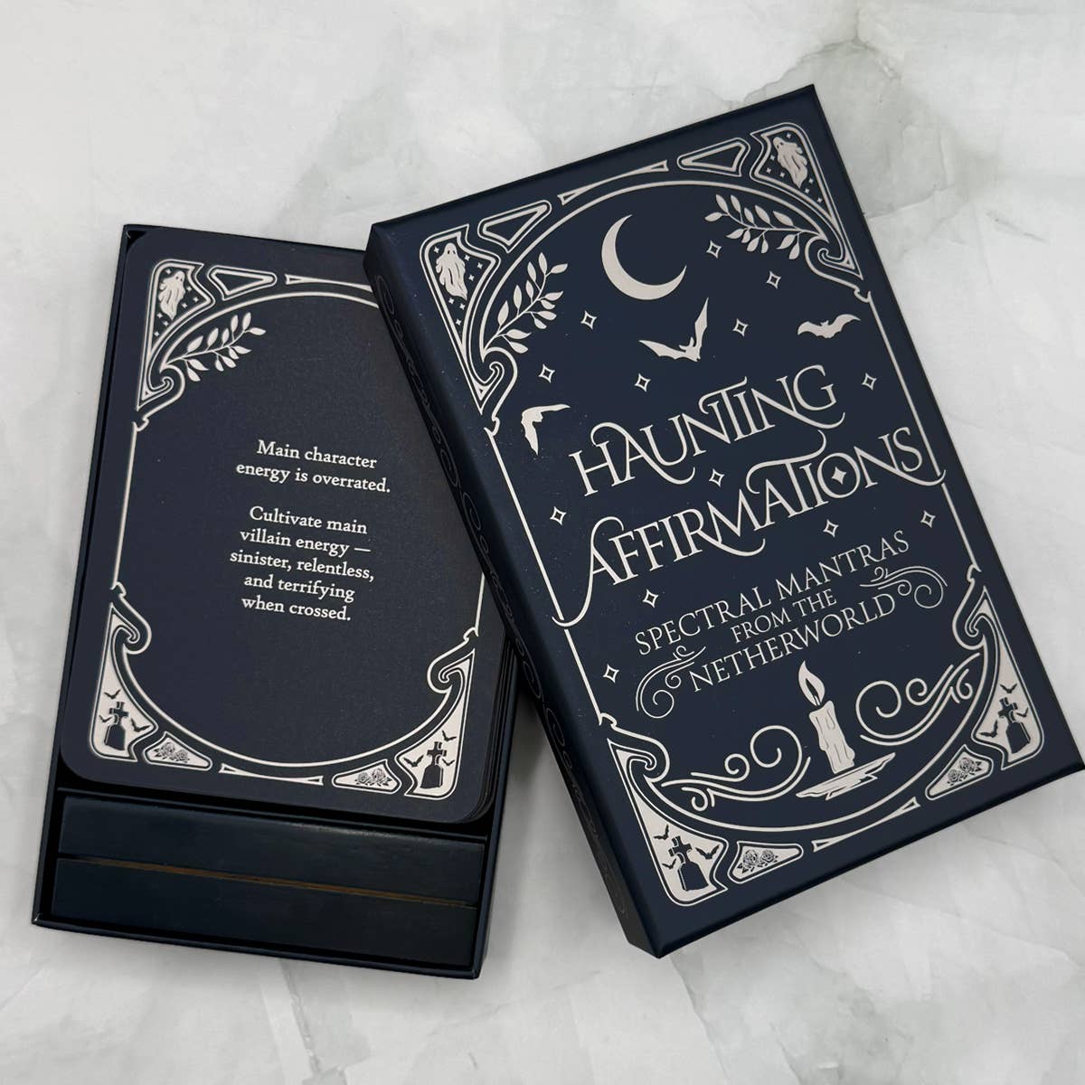 Dark blue card deck titled 'Haunting Affirmations' on a white marble surface