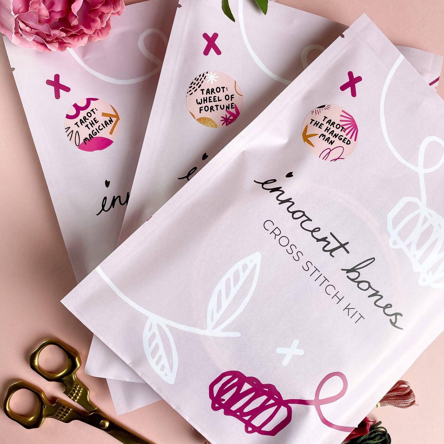 Cross stitch kit packaging with brand name and decorative elements on a pink background.