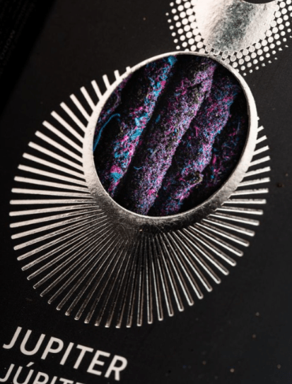Close-up of an incense stick box with a metallic design and colorful interior on a black background.