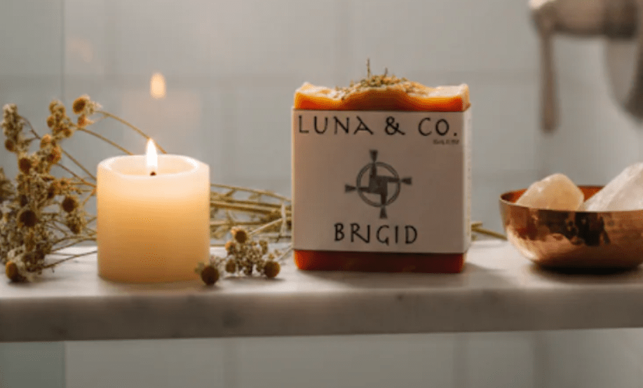 Bar of soap with 'Luna & Co.' branding next to a lit candle on a surface.