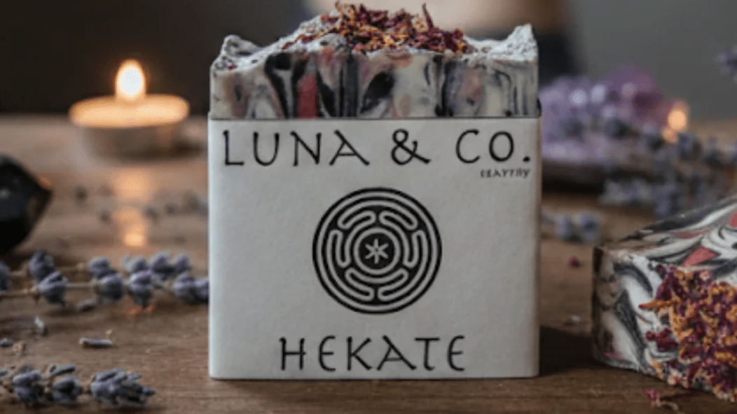Luna & Co. Hekate candle packaging on a wooden surface with decorative elements.