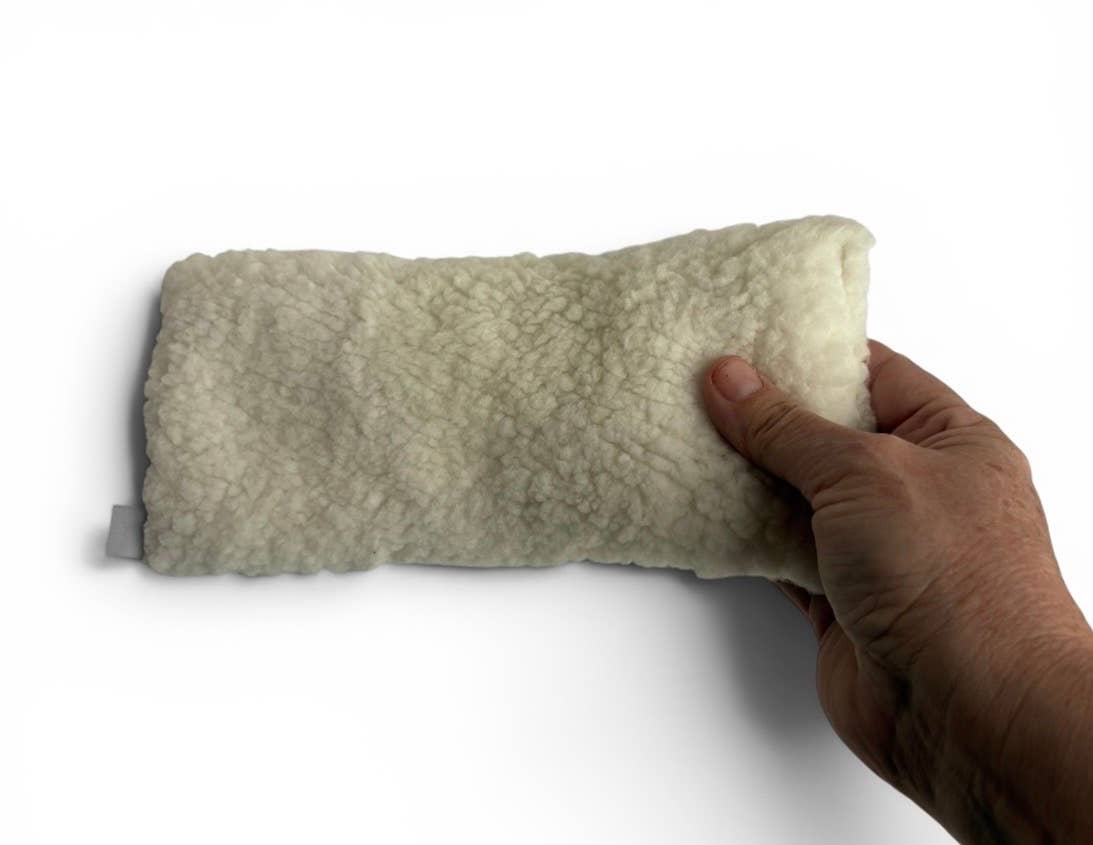 A hand holding a rectangular, cream-colored fleece or sherpa cushion against a plain white background.