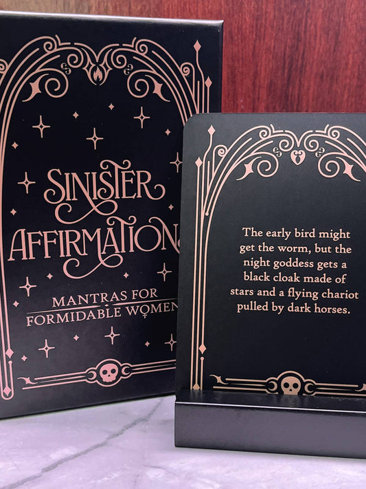 Black card with rose gold text and decorative elements on a wooden surface.