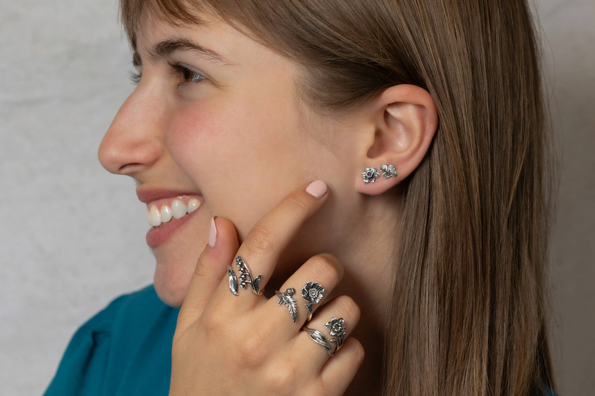Woman wearing silver earrings and rings, smiling against a neutral background