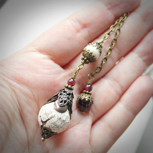 Pendulum with decorative beads held in a hand against a neutral background