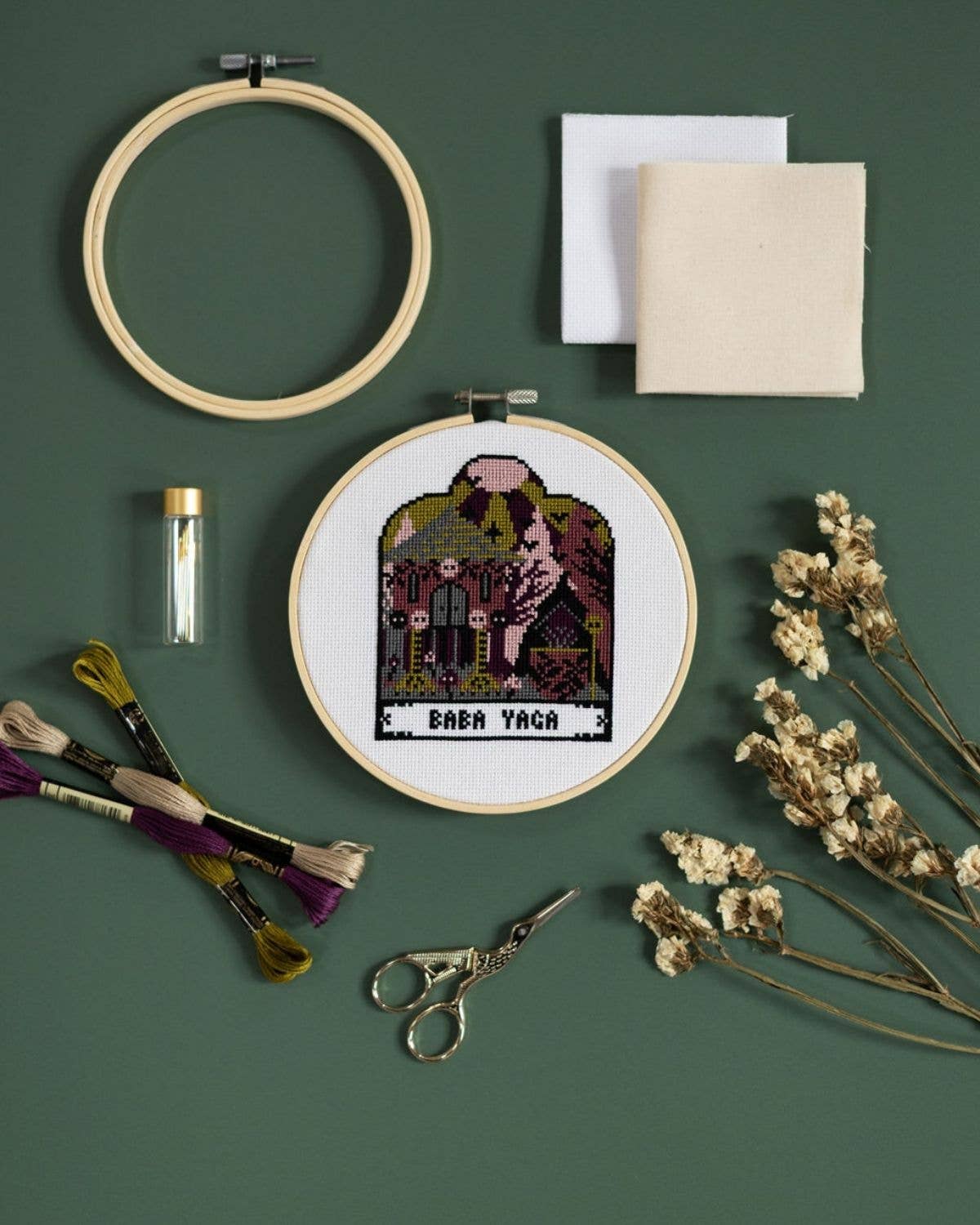 Embroidery hoop with cross-stitched design on a green background, surrounded by embroidery tools and materials.