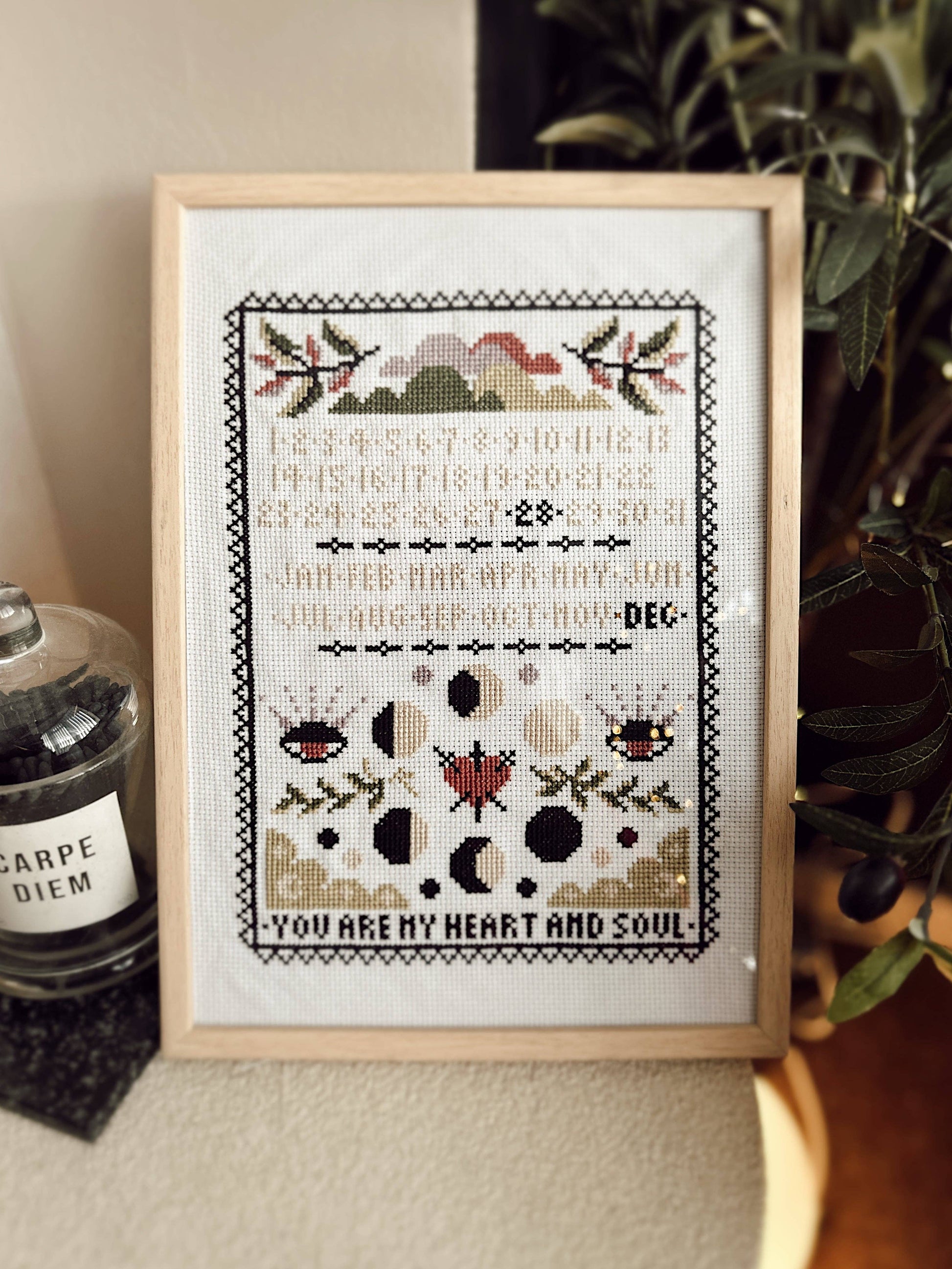Framed cross-stitch art with decorative elements and text on a neutral background