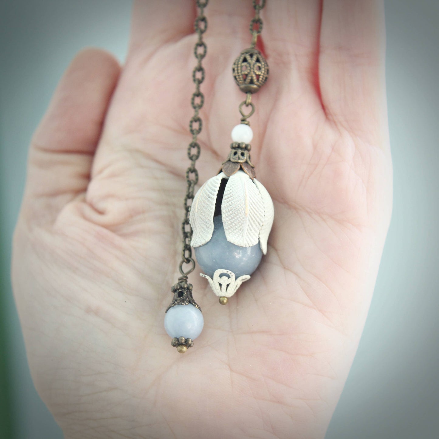 Pendulum with leaf-shaped stone held in a hand against a neutral background