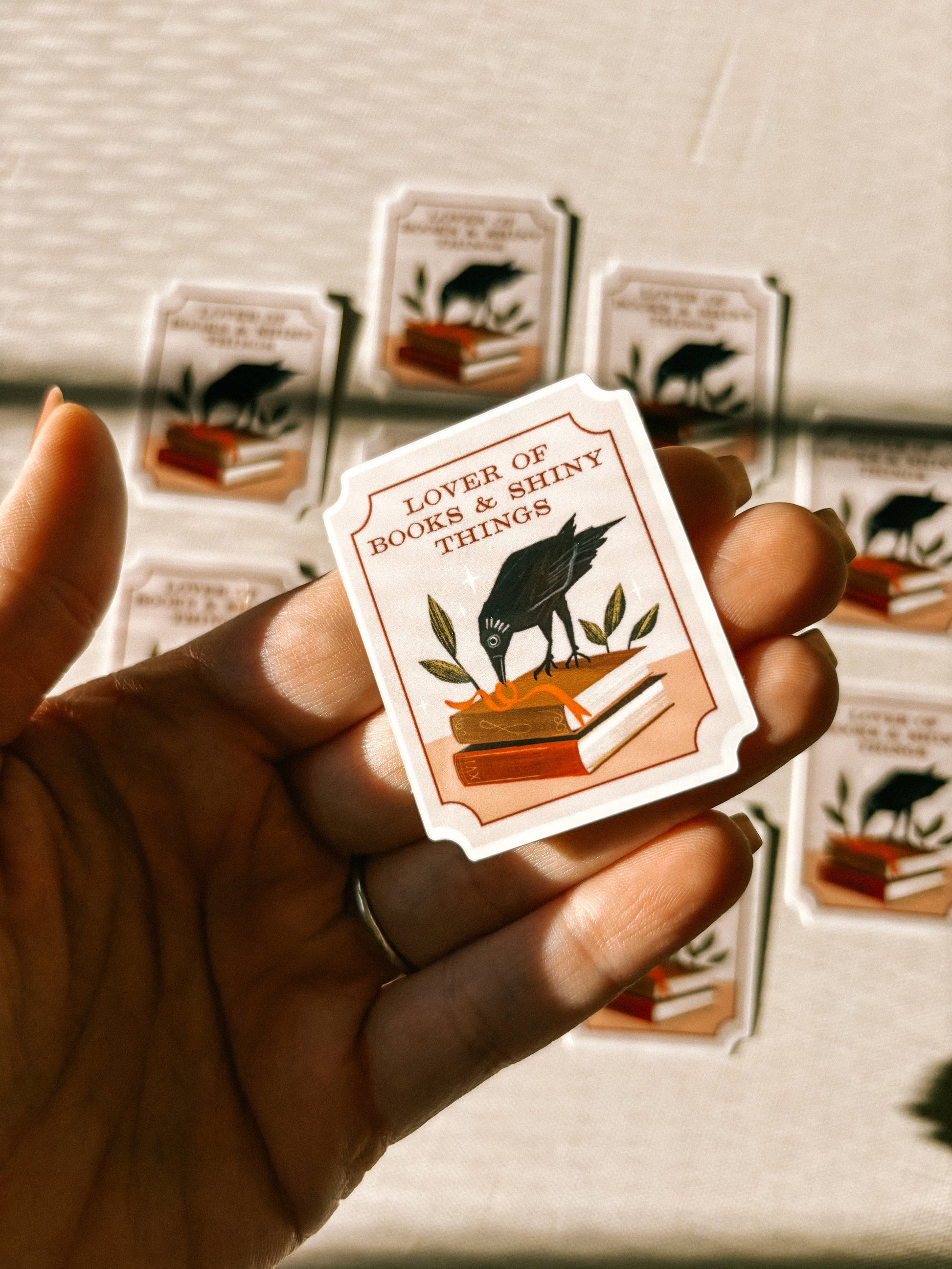 Hand holding a card with a design of a dog and text 'Lover of books & shiny things' against a blurred background.