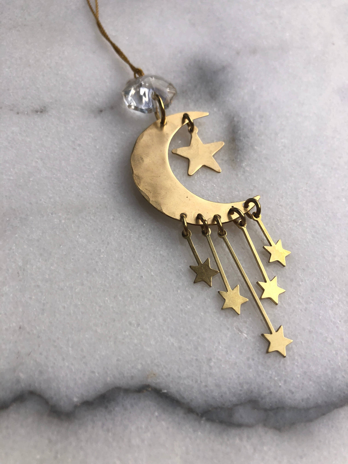 A gold crescent moon and star dangle necklace with a clear faceted bead, displayed on a light gray marble surface.