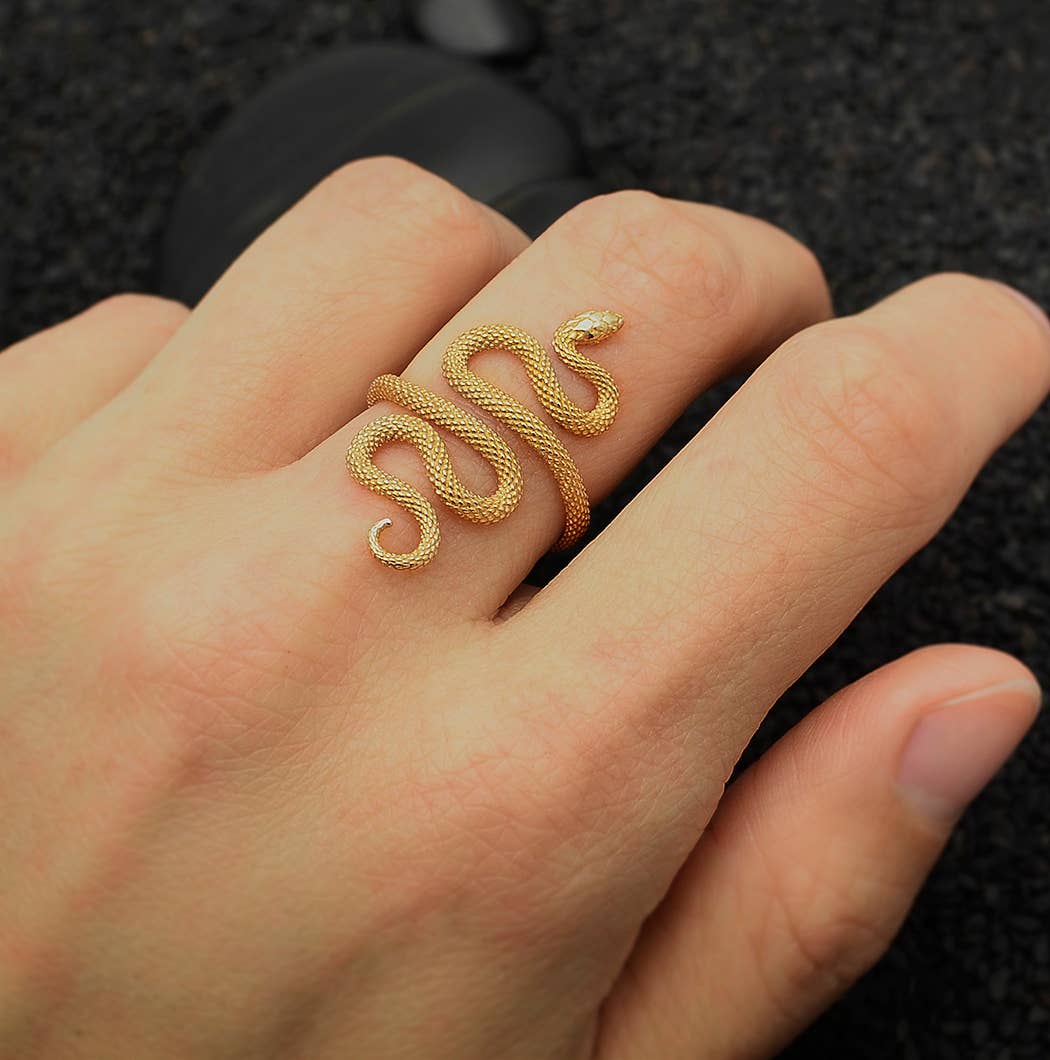 Gold snake-shaped ring on a person's finger against a dark background