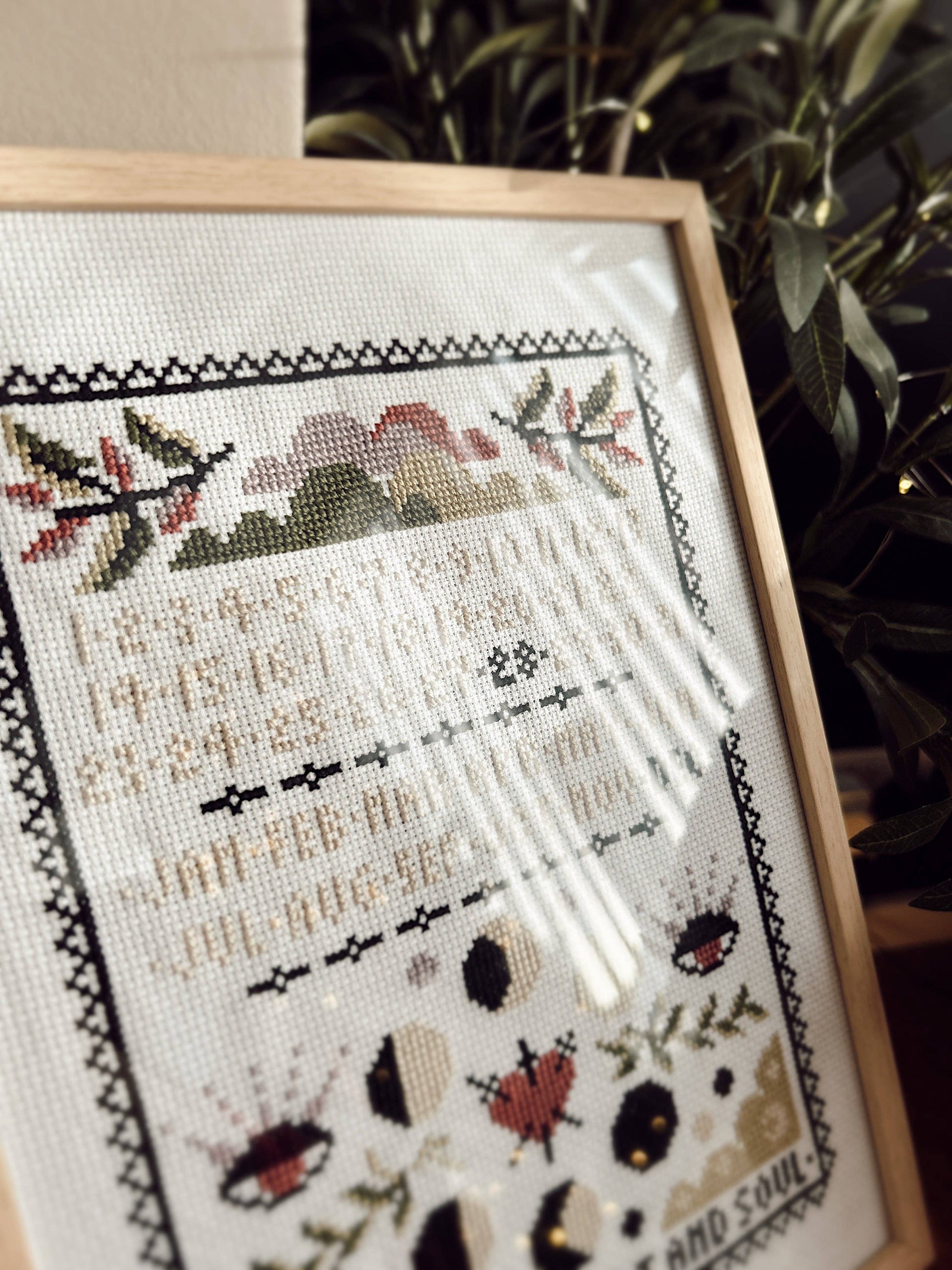 Framed cross-stitched piece with nature-themed design on a neutral background