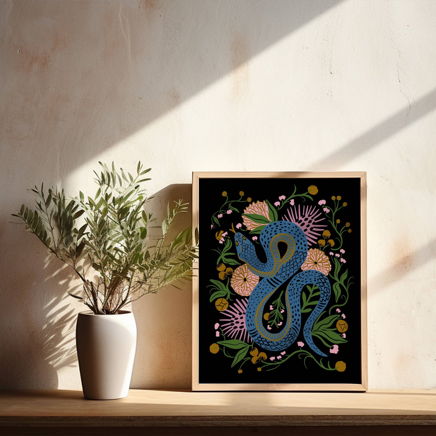 Charmed snake giclee print in a wood frame leaning against a wall.