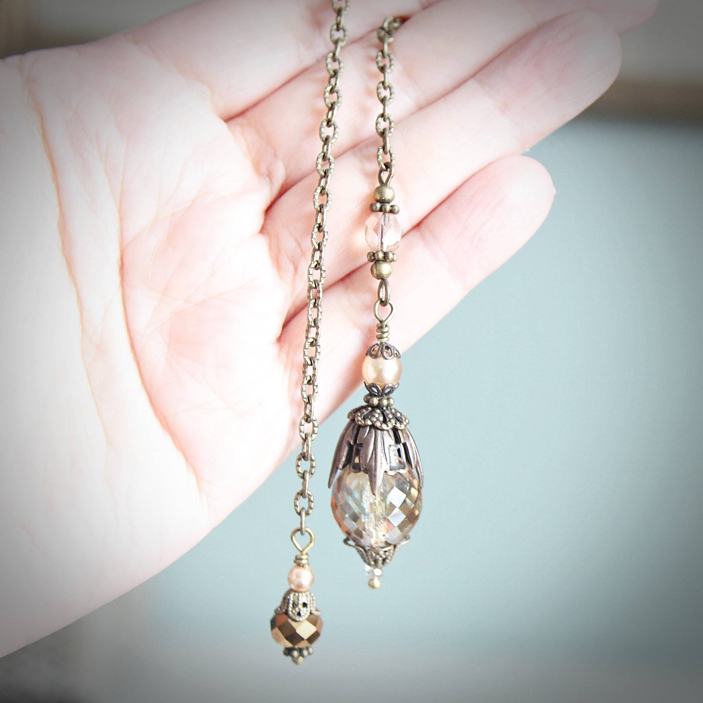 Pendulum with decorative pendants held by a hand against a blurred background