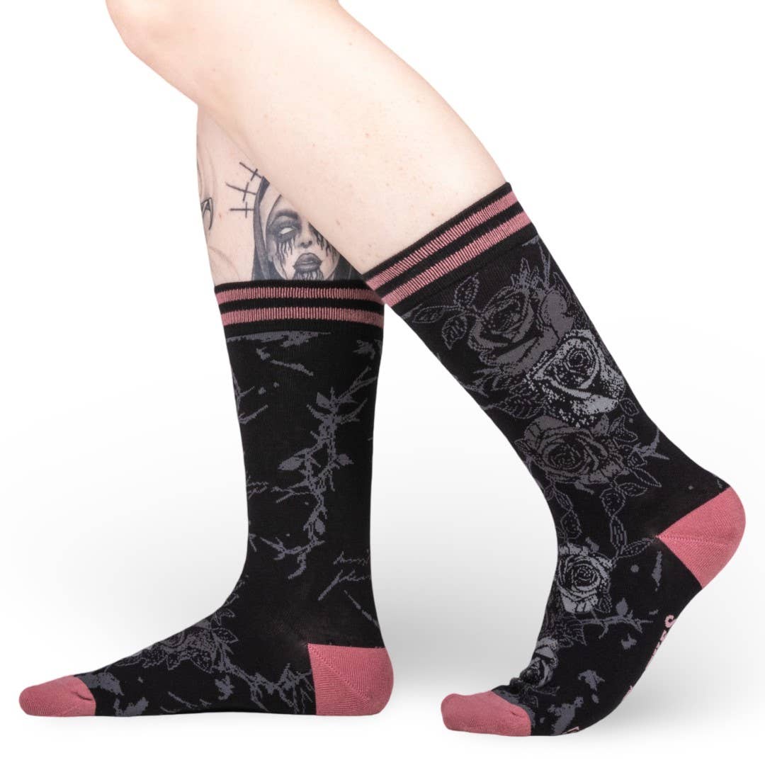 Black socks with floral patterns and pink accents worn by a person on a white background