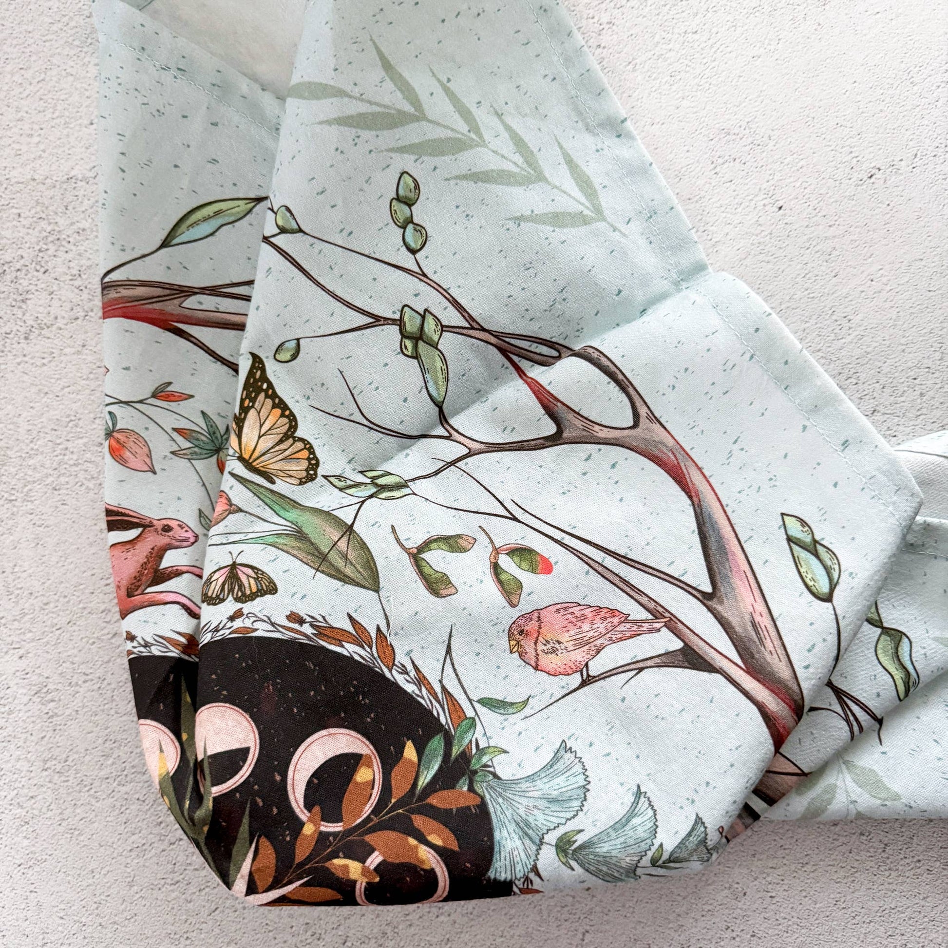 Folded fabric with nature-themed design featuring trees, birds, and butterflies on a light background.