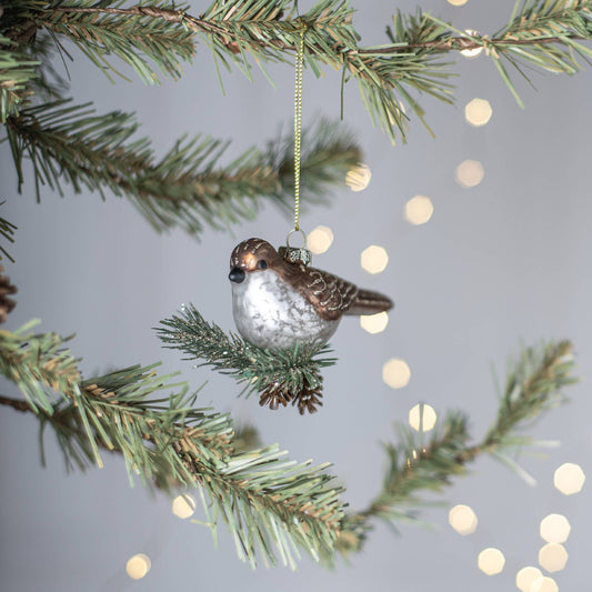Decorative bird ornament hanging on a Christmas tree branch with blurred lights in the background