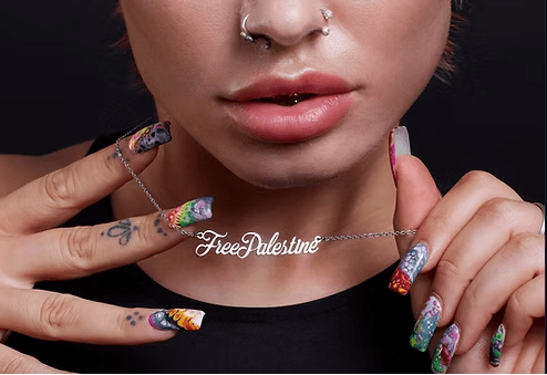 Close-up of a person with colorful nails and 'Free Palestine' necklace against a dark background
