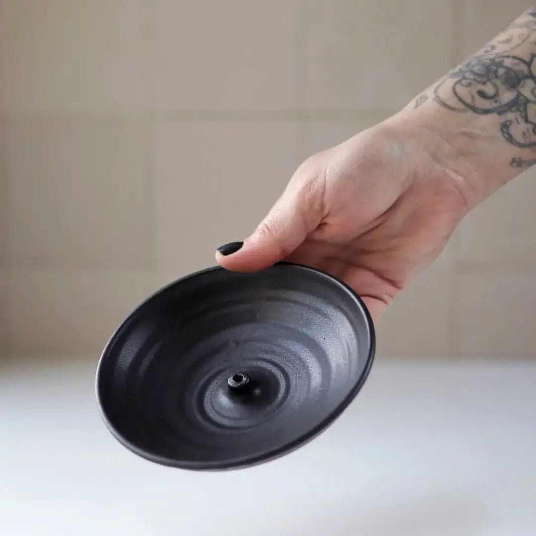 Hand holding a black ceramic bowl against a neutral background