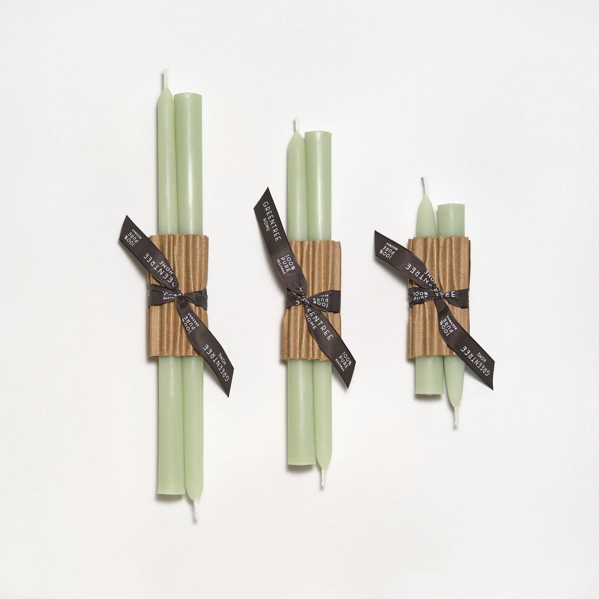 Three sets of green candles wrapped with brown paper and black ribbons on a white background