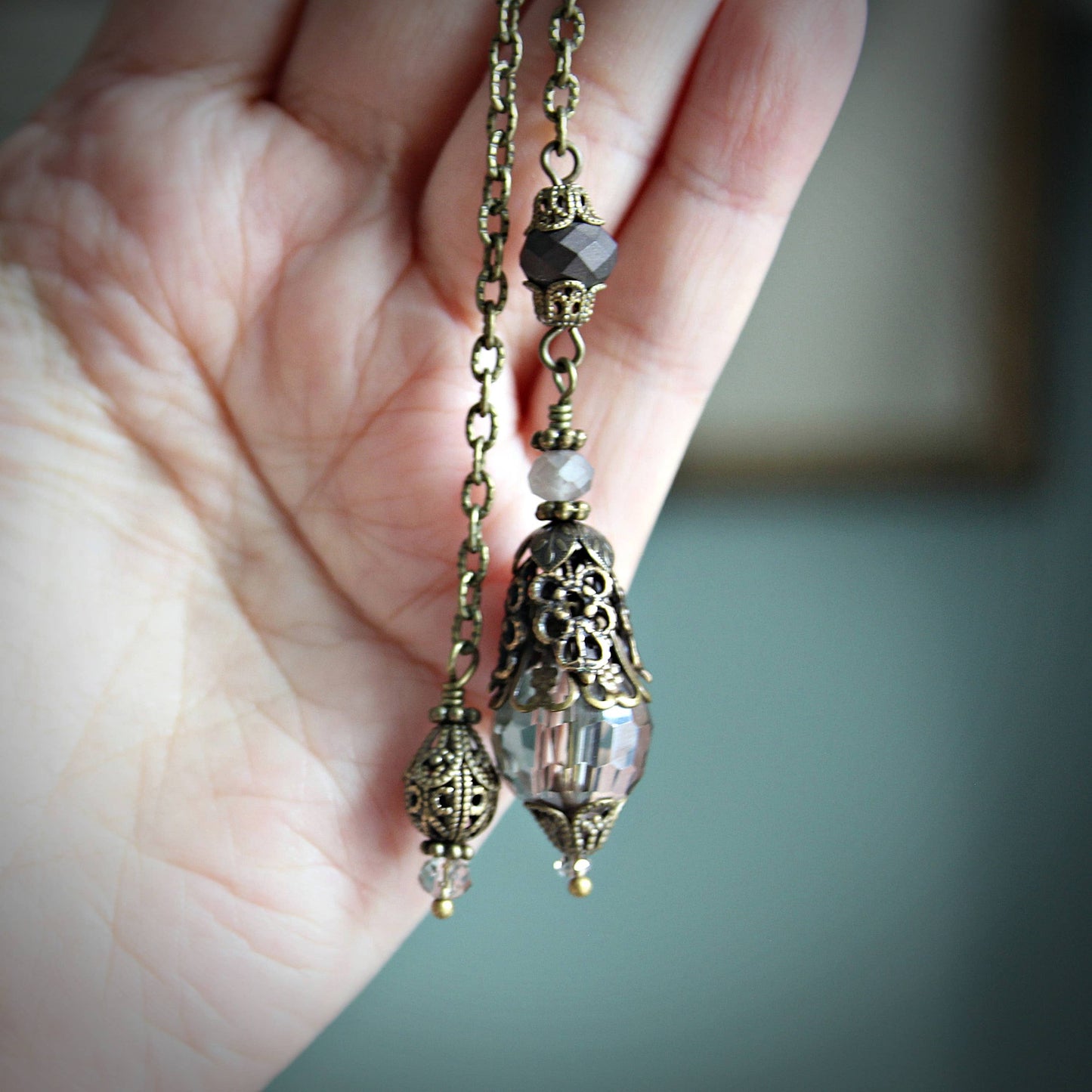 Hand holding a pendulum with ornate beads against a blurred background