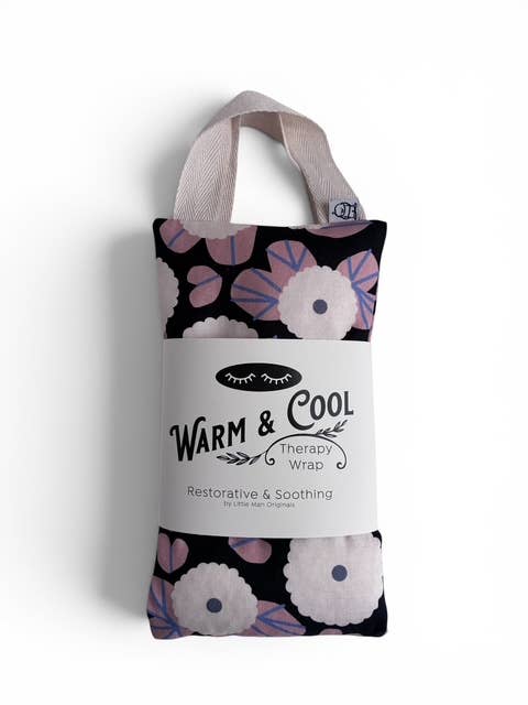 A packaged 'Warm & Cool' therapy wrap, a restorative and soothing self love cloth gift set. The product is shown folded with a black floral pattern, light pink and white flowers, and a light beige fabric strap.
