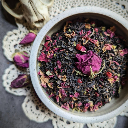 Tea leaves with pink and red flowers in a white bowl on a lace doily.