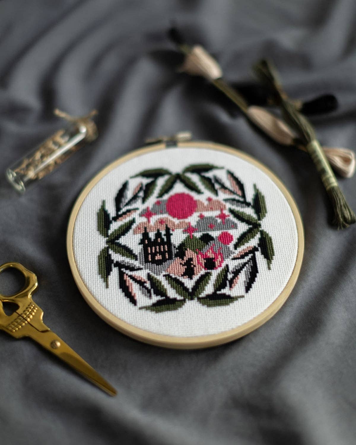Embroidery hoop with decorative cross-stitch design on a dark fabric background