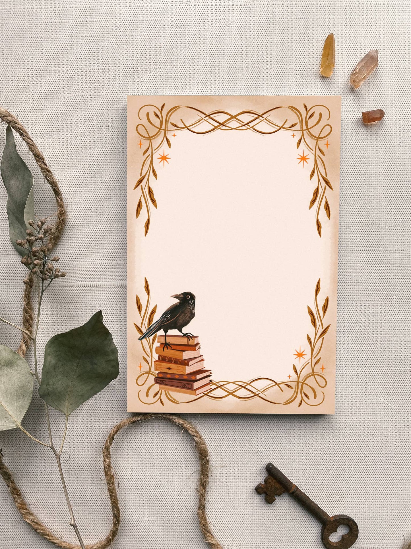 Decorative notepad with a crow on books design, surrounded by natural elements on a textured surface.