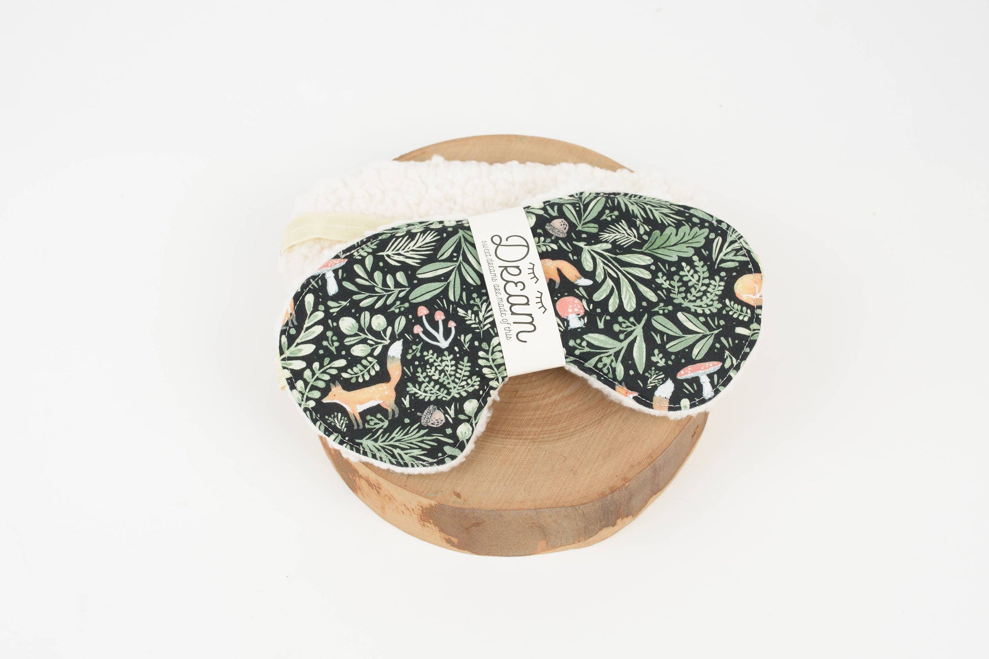Pair of green patterned eye masks on a wooden block with a brand label.