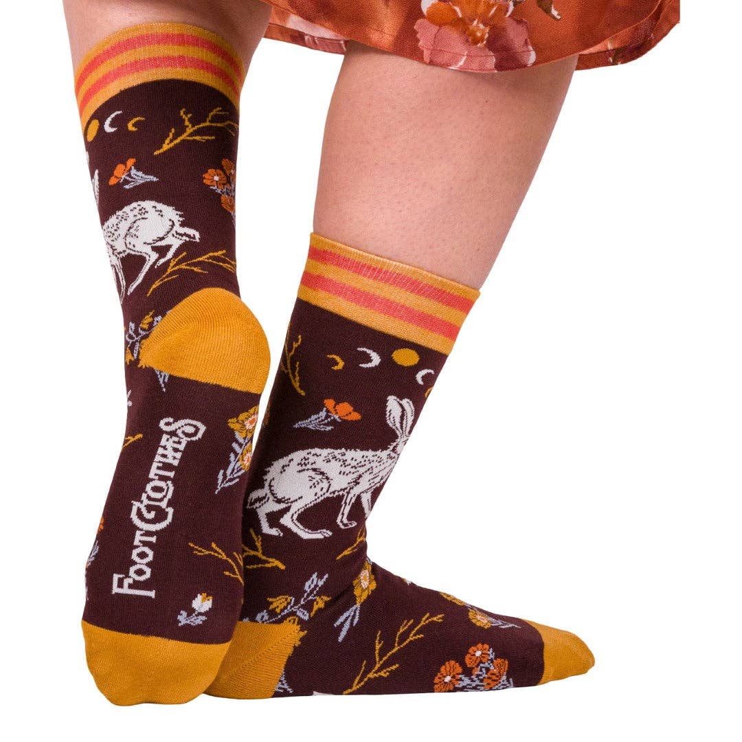 Pair of socks with a horse and moon design on a brown background, worn by a person.