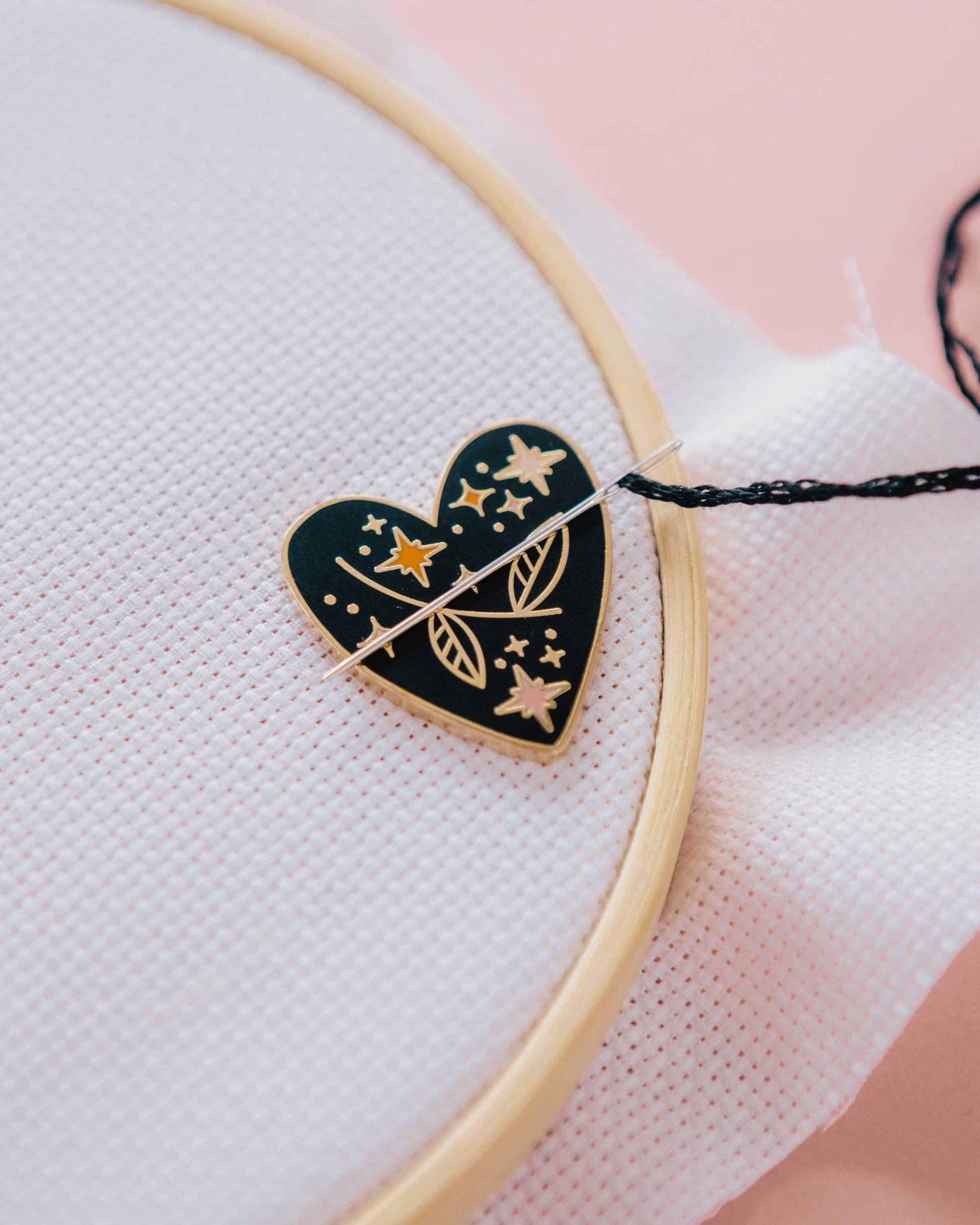Heart-shaped needle minder with star and leaf design on a white fabric background
